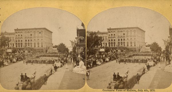 "From Sullivan's Block, outside Park Hotel, soldiers in a square," one of four "Different Views of Parades in the Streets" identified in Dahl's 1877 "Catalogue of Stereoscopic Views." The ceremonies are on the Capitol Square for the Centennial of the United States on July 4, 1876.  The view is looking toward the corner of Main and Carroll Streets.  Crowds line the streets waiting to see one of the four companies of the Illinois regiment "The Chicago Light Guard" who participated in the competitive drill. A hardware store can be seen in the background.