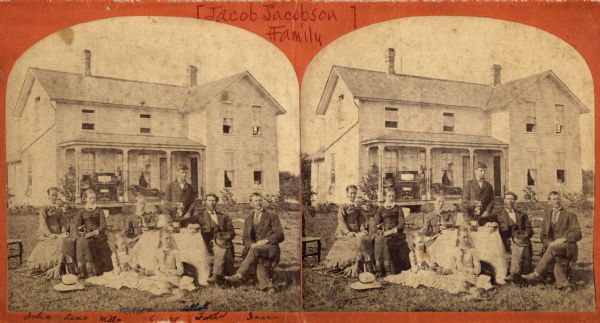 The Jacobson family sits with the dining table and dinnerware set up on the yard in front of their house. From left to right the family members are identified as: Julia, Lena, Milla, Mother, Clara(?), Abbot, Father and Inez(?). Clinton (?), Dane County.