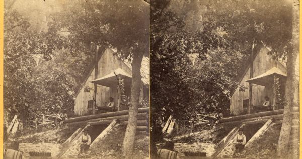 Three men rest outside a large cabin in a densely wooded area at Devil's Lake.