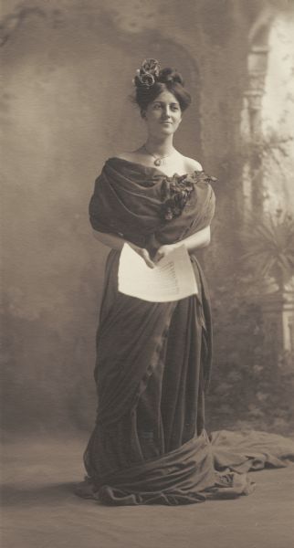 Emma Helen Strand, member of the Menomonie High School class of 1905, depicted as a contralto singer. Pictured holding sheet music. Part of a yearbook created by classmate Albert Hansen, based on a class prophecy theme.