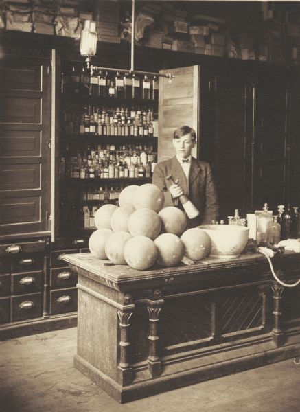 Fred Albert Quilling, member of the Menomonie High School class of 1905, depicted as a pharmacist, holding a large mortar and pestle. Part of a yearbook created by classmate Albert Hansen, based on a class prophecy theme.