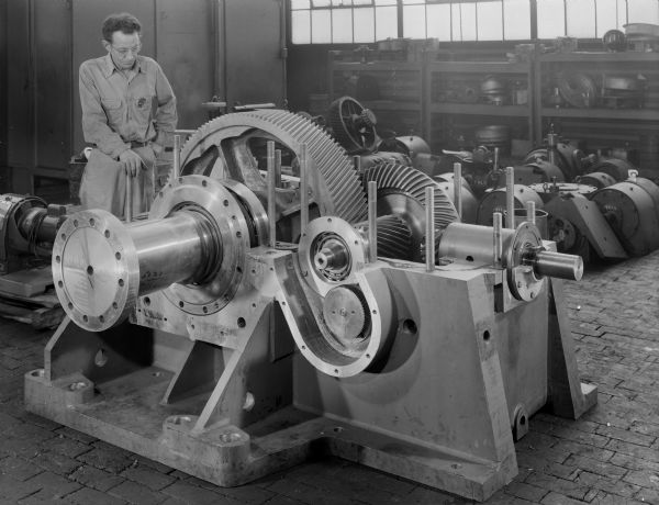 A male employee stands near a screw press washer. The speed reducer shown is a Right Angle, Double Red. Later purchased and used by the American Boxboard Company of Filer City, Michigan. Model Number, 5620-7166. Type of Unit, 11GDBTT.
Falk original caption reads: "Double row brings rated 100,000 hours average life, 1730-87.5 rpm; 19.795 ratio. 63,000 pound axial thrust. If one of these units goes out, whole plant is down."