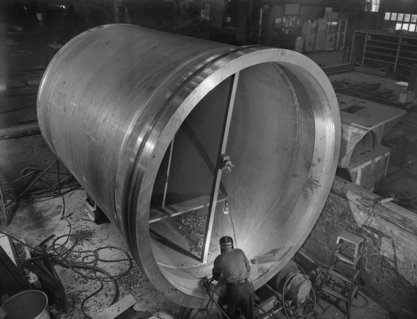 A man welds at the base of an upper chamber. This upper chamber or pressure vessel was purchased by Adamson-United Company of Akron, Ohio, and used by B.F. Goodrich of Miami, Oklahoma.
