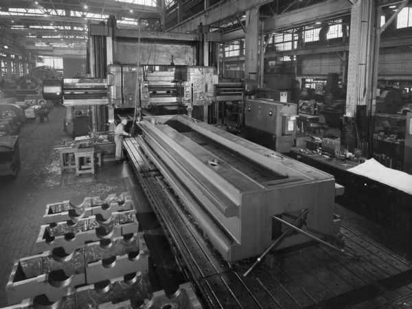 An employee stands near a cross rail that was later purchased by Onnsud Machine Works and used by Avco Corporation for cargo planes. Falk caption reads,"Machine wing sections for new type. 41 inches high x 91 inches wide x 324 inches long. Estimated rough weight 75,000 pounds. Finished weight 65,600 pounds (actual shipping weight)."
