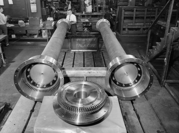 240P double piloted coupling. This coupling helps compile the centrifugal pump that was purchased by Foster Wheeler Corporation and later used by Commonweath Edison. Falk caption reads, "Vertical centrifugal pump application 2750HP motor at 300 rpm, with a distance of 30 feet between shaft ends. Gear box will be located on an upper floor and pump two floors below." The male employee in the photograph is James Kolbeck.
