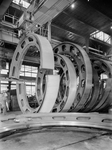 Eighteen foot split ring gear that is on display at the Falk Corporation. Falk caption reads, "Photos of ring gear to be displayed at Association of Iron and Steel Engineers (AISE) show in Cleveland, Ohio, September 26th through September 29th, 1966-including photos taken after painting and clean-up, but before wrapping in plastic. (See also EG 43235 and 43236). Approximate weight of 20 tons." Male employee is unidentified.