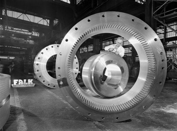 Coupling that was purchased and used by Sociedad Mixta Siderugia, a steel mill in Argentina. Falk caption reads, "This 240G coupling is largest Falk gear coupling furnished to date... this is part of a 1/4 million dollar batch of gear couplings to be installed in an Argentina steel mill." Male employee in photograph is D. Ferch.