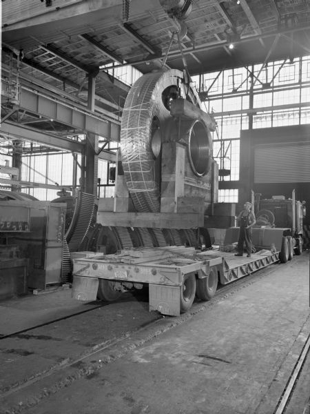 Bull gear for shaft on a BOF Drive. This gear was later purchased by Pennsylvania Engineering Corporation and used by Youngstown Sheet and Tube. Falk caption reads, "These photos taken for use as photo/caption release material prior to 1968 Steel Show. This gear, with four pinions fastened to it, constituted the predominant element in the Falk exhibit at the show." A male employee stands to the right of the bull gear.