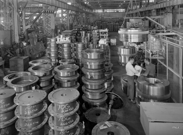 These couplings were later purchased by Mesta Machine and used by Republic Steel. Falk caption reads, "These photos [were] taken to illustrate various sizes of gear couplings being processed in the shop for [a] large Mesta order." Male employees in photograph are David Connell and Glorfield Kozlowski.