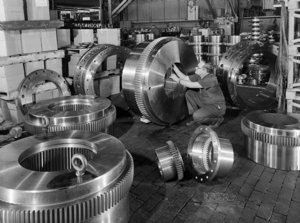 Various G couplings that were purchased by Mesta Machine Company and used by Republic Steel Company. Original Falk caption reads, "Various sizes of gear coupling hubs and sleeves above order in shop 2, 1/2 coupling area. The hub being miked by the inspector is size 260 G. The smaller coupling hub and sleeve in the foreground is size 70 G." Man in photograph is Roy Moldenhauer.