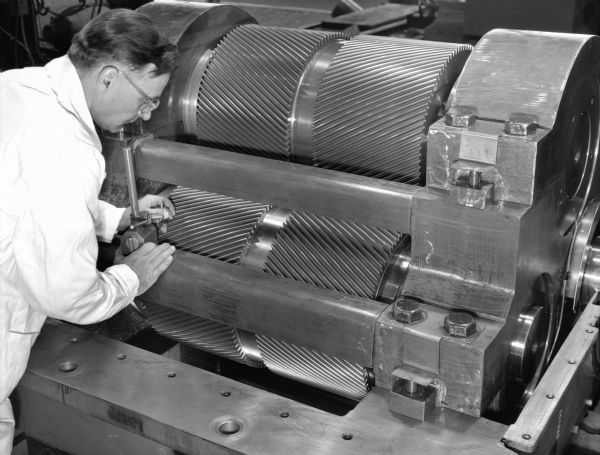 High speed gear unit that acts as a component in a gas turbine test-stand drive. This product was purchased and used by the Allison Division of the General Motors Company. Original Falk caption reads, "Falk primary and secondary high speed gear units furnished for test stand service... equipment includes Falk MOS. 6-775317, 318, 319. See Engineering File for exact details." Male employee in photograph is Vilas Kading.