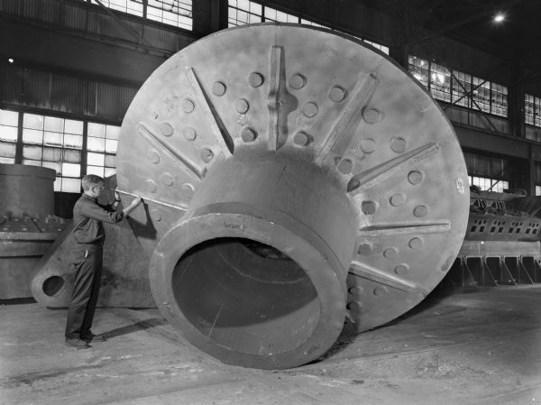 This product was later purchased by Fuller Company (Traylor Engineering and Manufacturing). Falk caption reads, "Estimated rough weight 46,720 pounds. Flange OD-12 feet-3 3/4 inches x 4 inches thick-5 feet one inch height. 5 feet 6 inch ODX 4 feet-2 inch ID of barrel. Flange of barrel 5 - 4 1/2 inch ODX 6 inches thick. Man in photograph is Ron Palmer."