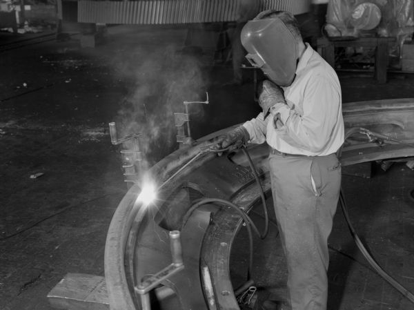 Male employee, John Beck, arc welding a mud guard to a split ring gear.