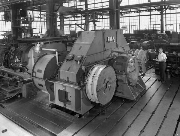 This two pinion combining gear, a component of a main propulsion system was purchased by Fairbanks Morse and used by Falcon Carriers Incorporated. Original Falk caption reads, "Main propulsion-35,000 DWT tanker. This FWD STBD quarter view of drive to combine two 7,500 hp pielstick diesels at 520 rpm and drive 110 rpm lineshaft. Note 39 inch thrust bridge accessories include clutches, brakes, quill drive and complete lubrication system. See Engineering File for exact specifications." Male employee in photograph is W. Steffen.