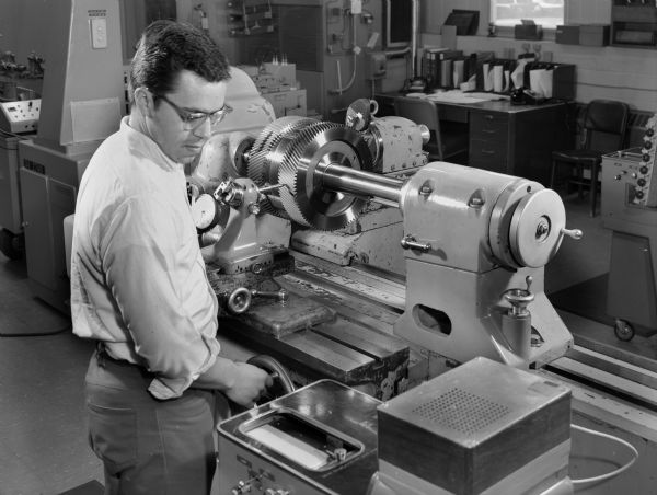 A male employee, Dennis Zastrow, inspects a gear in the gear lab.