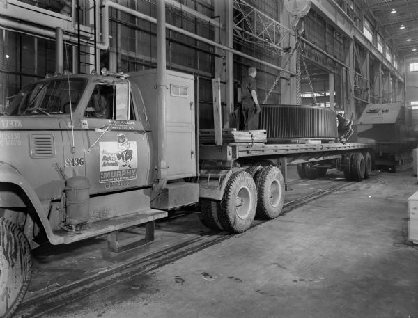 View of a 29 foot in diameter ring gear that is a component of a ball mill drive on a truck. This ring gear was purchased by Koppers and used by Hannah Mining. Original Falk caption reads, "29 foot diameter, 31 inch face single helical split ring gear... see Engineering File for exact specifications." Male employees in photograph are Ken and Roger Knudson.