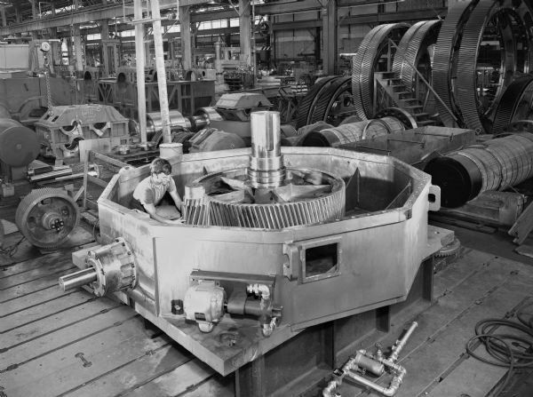Speed reducer that is a later component of a coal pulverizer. This product was purchased by the Foster Wheeler Corporation and used by the Public Service Company of San Juan Station, New Mexico. Original Falk caption reads, "4 units furnished 2197ZBX2-S speed reducer, double red right angle, horizontal input shaft, vertical up output shaft, 780 rpm in, 27.6 rpm out, ratio 31.417:1, service rating 537 hp, S.F.=1.5. Order included a portable turning gear and 140T35 HS couplings." Male employee in photograph is Tom Wolf.