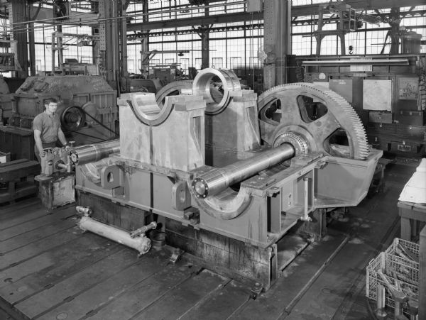 View of a speed reducer that was purchased by the Kennedy Van Saun Corporation and used by Gresic Cement in Indonesia. Falk caption reads, "Design HP-3150, service hp-2100, service factor-1.50, input rpm-600, output rpm-17.321, ratio 34.640:1." Male employee in photograph is Dick Gregory.