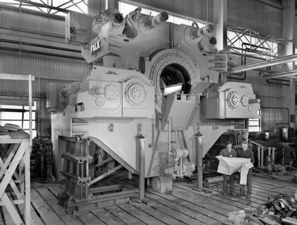 Shaft mounted BOF drive that was a later component of a basic oxygen furnace tilting drive. This product was purchased by Ferrostaal AG of West Germany and used by Somisa of Argentina. Falk caption reads, "SM, SM, BOF drive (2 units furnished) see Engineering File for exact unit specifications." Male employees in photograph are E. Grown and David Dupree. 
