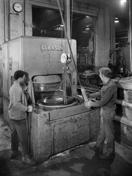 Original Falk caption reads, "Largest bevel gears manufactured by Falk to date. This photograph was taken in the Heat Treat Department." Male employees in photograph are Wayne R. Ziolkourk and Leroy Jackson Jr.