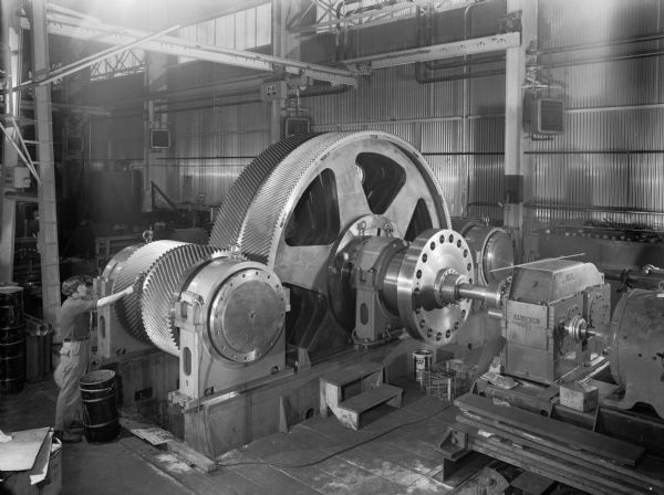 Special speed reducer that is a component of a larger Ozark Unit with L.S. pinions that is used as a dam generator drive. This unit was purchased by Allis Chalmers and used by the United States Corps of Engineers. Falk caption reads, "Low speed gear and pinions for second last Webbers Falls unit on Lapper in Shop 4." Male employee in photograph is Jose Ojeda.