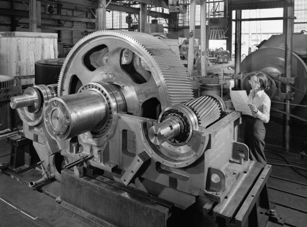 Twin pinion marine red gear that was used by The Offshore Company for the Discoverer 534, a deep ocean drilling rig. Original Falk caption reads, "Propulsion gear [for a] deep drilling rig drive by four-2000 horsepower reversible motors (pinion shafts are double ended) through 55G20 or 55G52 couplings. Eaton 60VC1600 brake on LSS stops propeller before motors are reversed. Unit has all anti-friction bearings and is rated for ABS ece ceass 1A. Lube system includes a MR type gear drive[n] [by a] main lube oil pump, plus a motor drive auxiliary. When the ship is drilling in the North Sea and the oil temperature drops below 60 degrees Fahrenheit, the thermostat turns on the heater, the motor driven pump and also energizes a solenoid valve which directs the oil flow from the cooler to the heater." Female employee in photograph is Katy Exner.