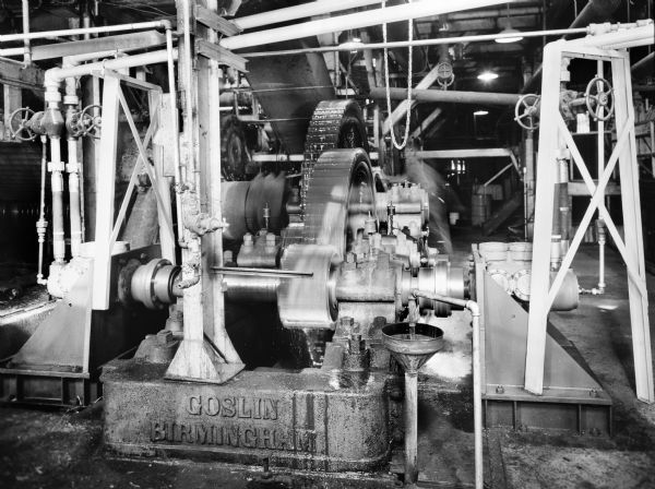 Fluid power drive that was a later component of a sugar crusher drive. This unit was purchased by Voorhies Supply and used by Glenwood Sugar Cooperative. Original Falk caption reads, "This was the 'first' hydraulic crusher drive ever installed in a sugar mill. Its overall performance was successful during the first season of operation." The blurred image of a man can be seen working in the background.