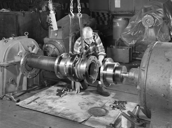 A male employee, Al Arndt, attends to a slide coupling. This particular coupling was purchased and used by Blaw-Knox. Falk caption reads, "Photos of a special slide coupling. Size 50GL32S... See Engineering File for exact specifications. Assembly drawing 424364."