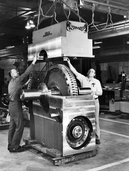 Two Falk employees, Arthur Hirt on the left, and Karl Becker on the right, attend to a large gear. This particular unit was purchased and used by United States Steel. Original Falk caption reads, "Cover off views of a 280BUD worm gear unit at Falk Tool."