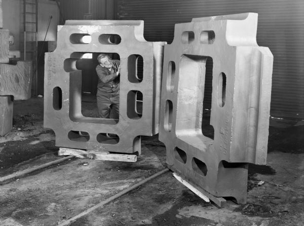 A Falk employee, George Cira, inspects the components of a later ejection box. This unit was purchased by Central Foundry, a division of the General Motors Company. Original Falk caption reads, "Ejector box, pattern number CFB-4916-3. Approximate weight 12,500 pounds, material: Falk Gear alloy number 4, N and T to 269-309 BHN."