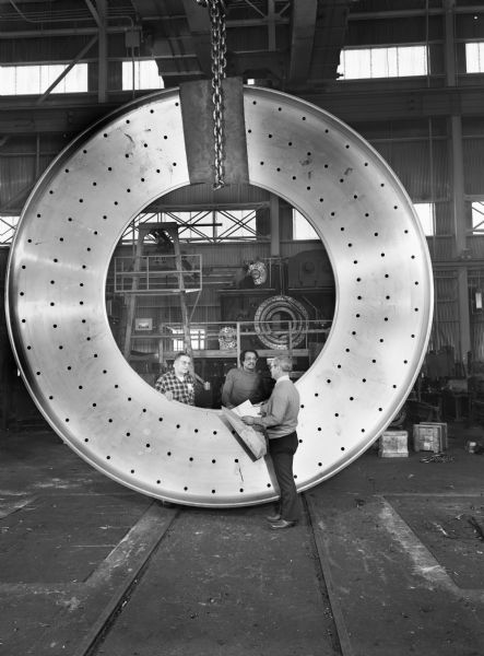 A Falk employee, John Bartaczewicz, inspects a large inlet head. This particular unit was purchased by F.L. Smidth and Company. Original Falk caption reads, "Inlet head (better known as a frisbee). Pictures show finish machine frisbee during final inspection. Pattern number DXL-241; estimated rough weight 30,870 pounds, material ASTM A27 Gr. 60-30, diameter approximately 30 feet."