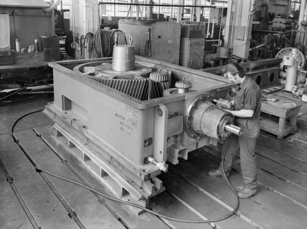 A male employee, Michael Nycz, attends to a pulverizer mill that is a later component of a coal pulverizer. This unit was purchased by Foster Wheeler and used by Teurel Power of Spain. Original Falk caption reads, "This unit is one of eighteen units going to Spain. Unit is designed to carry a thrust load of 427,000 pounds on low speed shaft."