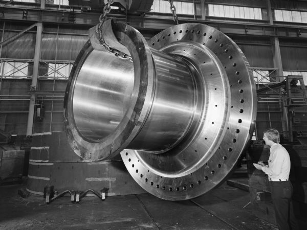 William Rhody, a Falk employee, inspects a large, floating trunnion. This particular unit was purchased by Humboldt-Wedag. Original Falk caption reads, "Finished machined and drilled trunnion. Pattern number E408-16-703EA. Approximate rough weight 89,700 pounds, material-Falk Gearalloy number 1 N and T. Important dimensions: large flange O.D. 12 feet 5.6875 inches, height 6 feet 7.875 inches, small flange O.D. 7 feet 10.5 inches, bore-63.797 inches, diameter barrel O.D.-6 feet 9.125 inches."