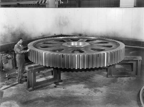 Anotha Burt, a Falk employee, inspects a large walk gear. This particular gear was purchased by Page Engineering. Original Falk caption reads, "Large walk gear pattern number 95599, approximate rough weight 60,000 pounds, approximate final weight 43,000 pounds, material 4335 N and T 240-280 BHN O.D. 168 inches. Photos show subject gear, finished machined, and with the teeth cut being prepared for shipment."