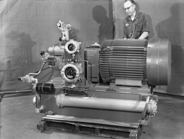 Art Hirt, a Falk employee, inspects a large mixer drive. This unit was purchased by the Mixing Equipment Company. Original Falk caption reads, "Picture taken at the Falk Tool Works. F.P.G. has immersion heater, dual suction filters-26 PV with P-70 actuator and P.O.R valve, gauges, explosion proof lever switch, temp SW, pressure sw, vacuum sw, side view, actuator side of pump and beveled motor mounted on 2445 RTS."
