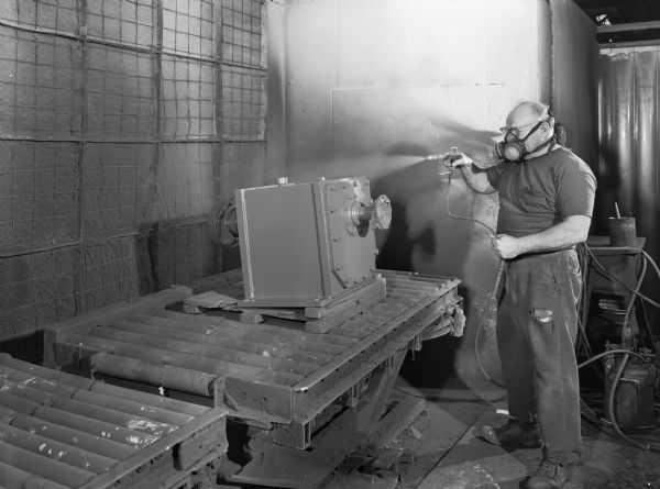 Original Falk caption reads, "A series of photos to illustrate various manufacturing operations for future publications: Also color for slide talks." Male employee in photograph is George Jenders, spray painting.