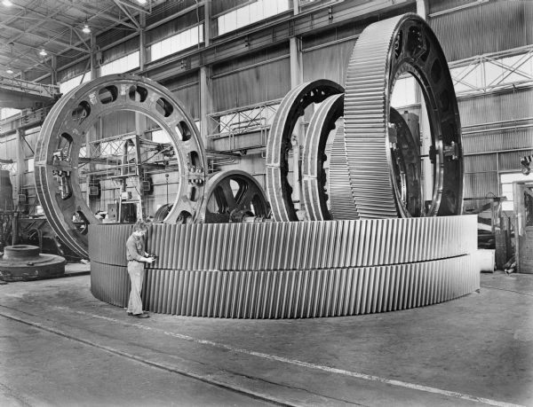 Original Falk caption reads, "General run of the mine large ring gears in various stages of manufacture waiting for subsequent machining operations. This series taken for possible use as Glamor "Large Gear" illustrations." Male employee in photograph is James Clark.