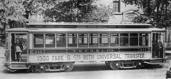 A T.M.E.R. and L Company streetcar is stopped on Washington Avenue, with the two streetcar operators aboard. The advertisement on the streetcar reads, "1900 Fare 5 cents with Universal Transfer." Original Falk caption reads, "Photos borrowed from Milwaukee County Transport for use in brochure 850801. Originals returned to County. Milwaukee streetcars."