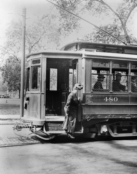 A woman carefully steps off a Milwaukee streetcar. Original Falk caption reads, "Photos borrowed from Milwaukee County Transport for use in brochure 850801. Originals returned to County. Milwaukee streetcars."