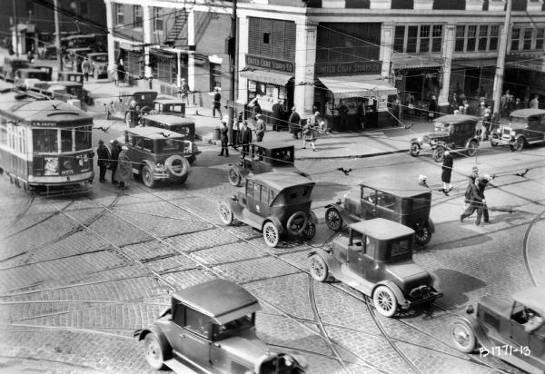 Busy street in Milwaukee, bustling with automobiles, pedestrians, and a streetcar. Original Falk caption reads, "Photos borrowed from Milwaukee County Transport for use in brochure 850801. Originals returned to County. Milwaukee streetcars."
