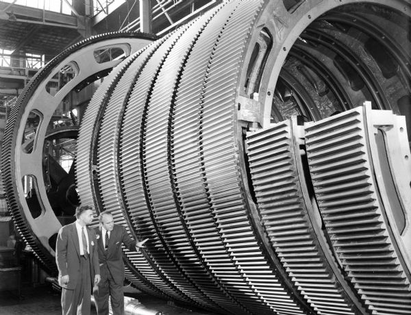 Two unidentified Falk employees inspect a large gear. Original Falk caption reads, "Centennial historical photos of old negative which could be lost forever. Probable period 1950-1960."