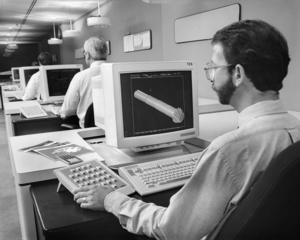 An unidentified Falk employee views a technical drawing on a computer screen. Original Falk caption reads, "Person in CAD room looking at CRT screen with marine drive showing."