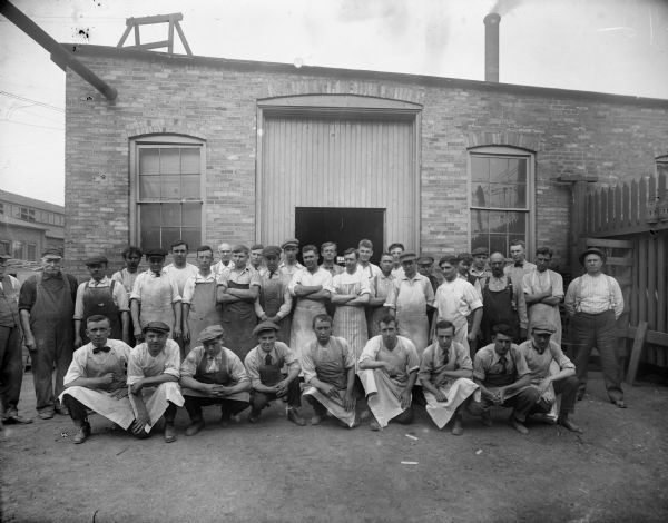 Male employees of Falk pose for a group portrait outside of the factory. Original Falk caption reads, "Centennial historical photos of old negative which could be lost forever. Probable dates prior to World War One."