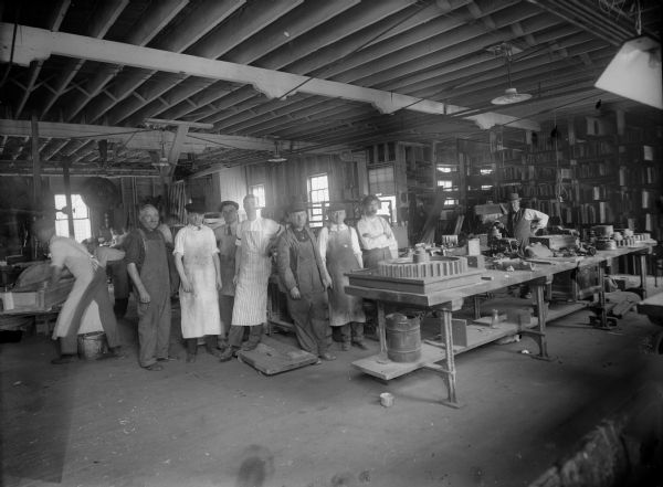 Several male employees gather in the factory. Gears and other machinery is visible. Original Falk caption reads, "Centennial historical photos of old negative which could be lost forever. Probable dates prior to World War One."