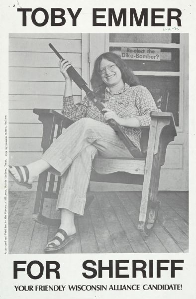Poster supporting Toby Emmer for Sheriff in Dane County, endorsed by the Wisconsin Alliance. Features a photograph of Emmer sitting in a rocking chair on a porch holding a rifle. She was running a protest campaign.