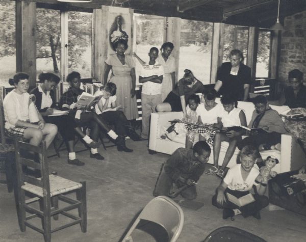 Koinonia Youth Camp in the Highlander Library at the Highlander Folk School.  The woman in the background is identified as Septima Clark. Koinonia is a farm in Georgia that was holding integrated children's camps when they were not allowed to do this in Georgia, Highlander let them come to Summerfield, held for two years, 1956 and 1957.