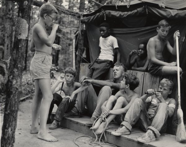 Group of boys and one man relaxing in a lean-to at the Highlander Folk School, behind the nursery school. Part of Koinonia Children's Camp. David Tate seen on the far right.