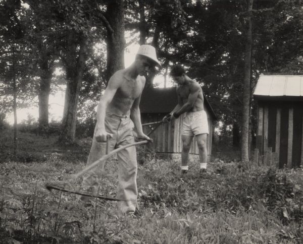 Two work campers at the Highlander Folk School cleaning the school grounds. The boy in front is using a scythe to clear brush.