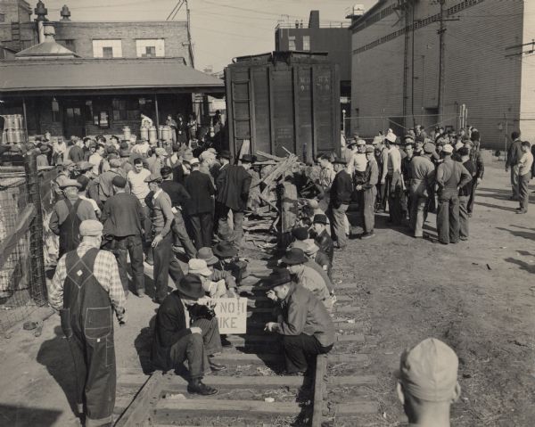 Strike of Chattanooga Packinghouse Workers.  A number of workers, one holding a picket sign, are sitting on a railroad track.
