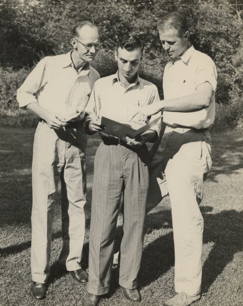 Unknown group of three men looking over a pamphlet at Highlander Folk School.